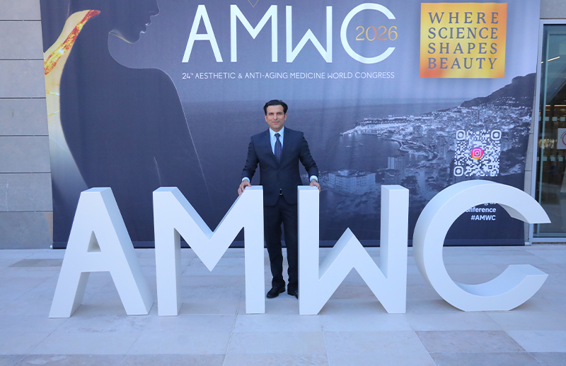 Dr Bilal Malik standing at AMWC Monaco entrance with large AMWC sign